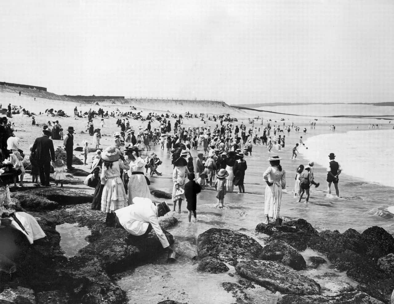 People in suits dresses and hats standing near water and rocks