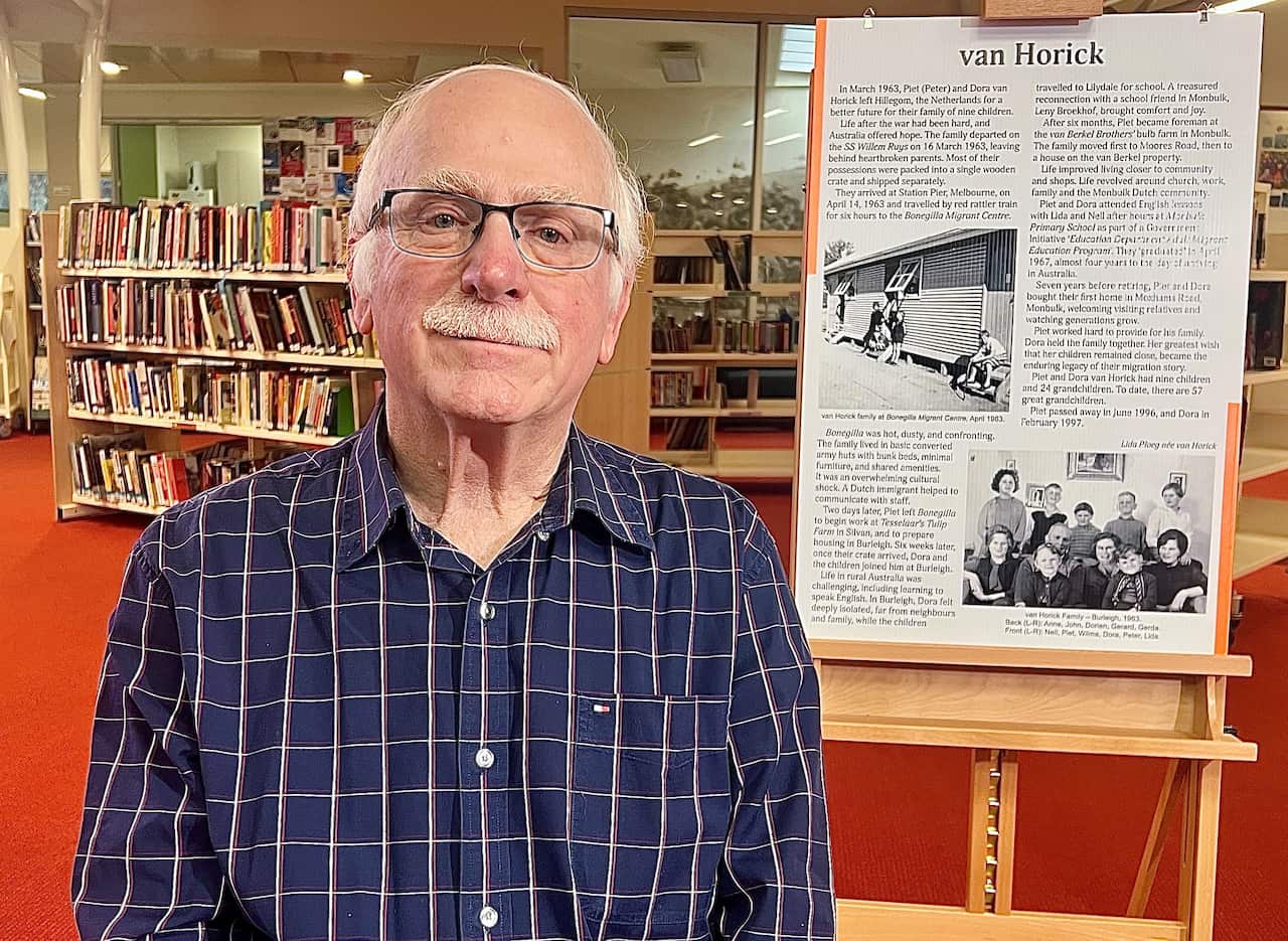 A man wearing glasses and a blue checked shirt sits in front of a story board in a library.