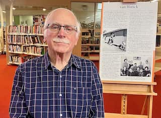A man wearing glasses and a blue checked shirt sits in front of a story board in a library.