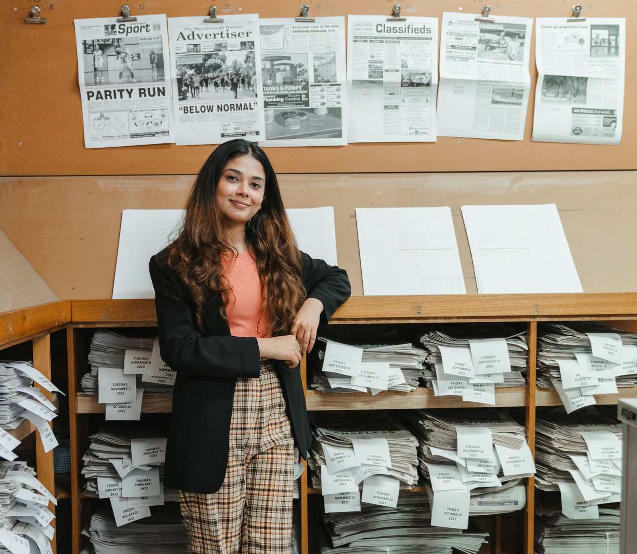 A young woman standing in front of piles of newspapers