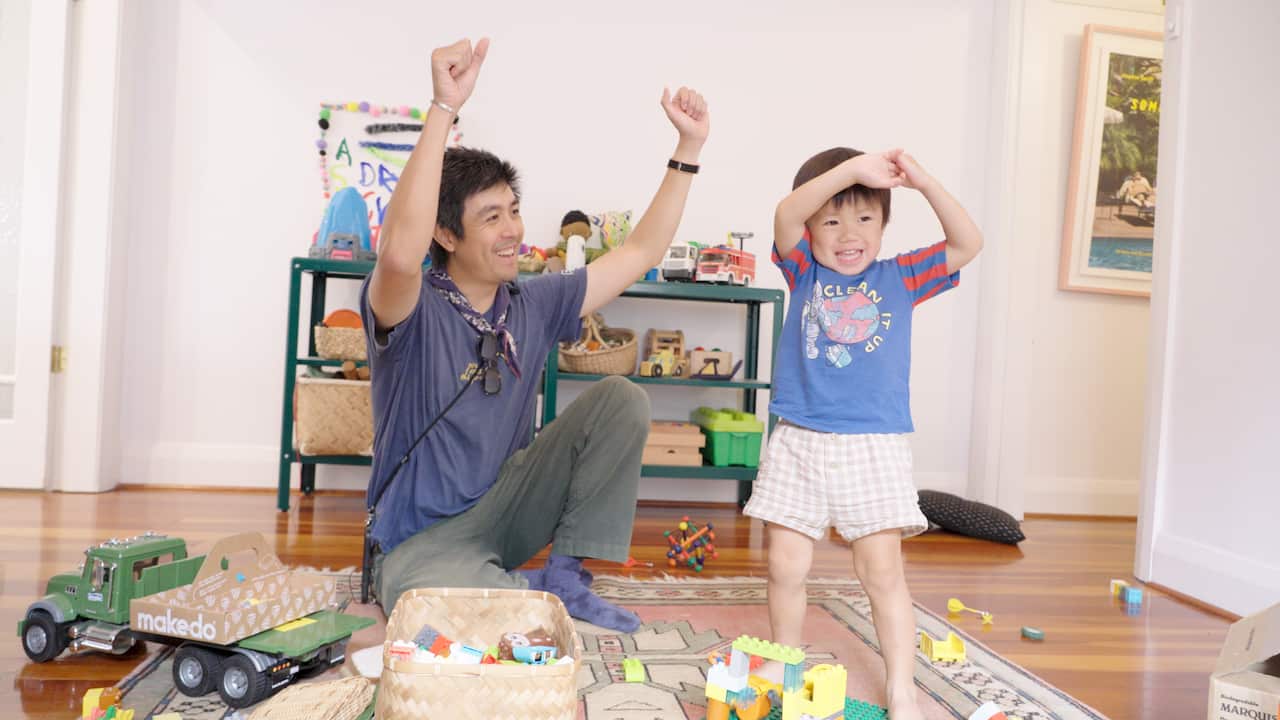A father and his son are throwing their hands up in the air in celebration in their living room