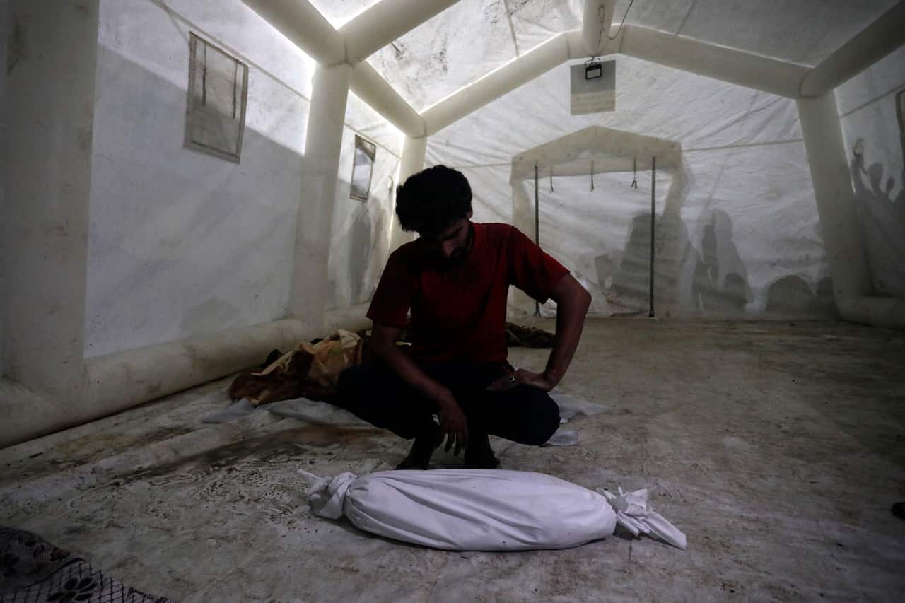 A man crouches over the body of a child wrapped in a shroud