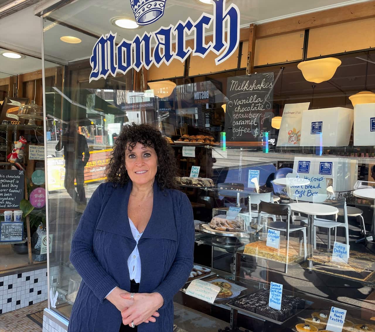 A woman in a blue cardigan standing outside the window of a cake shop.