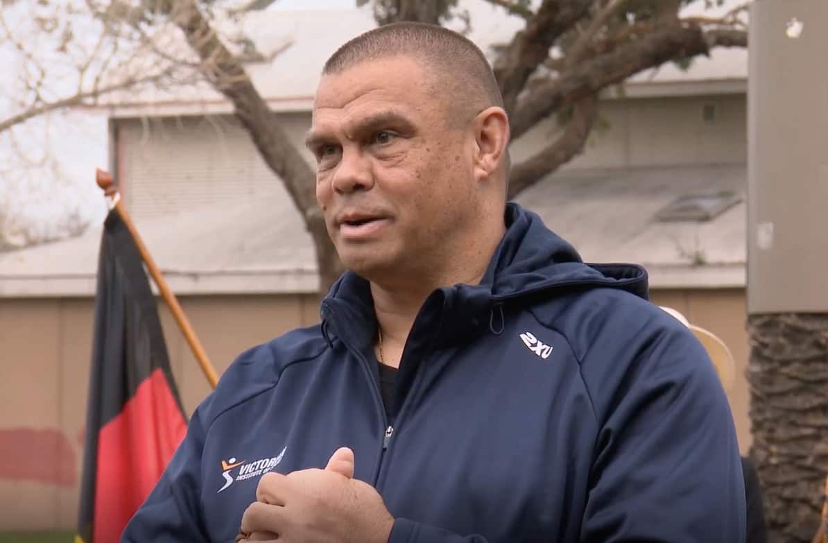 Kyle Vander-Kuyp standing in front of an Aboriginal flag, speaking to media.