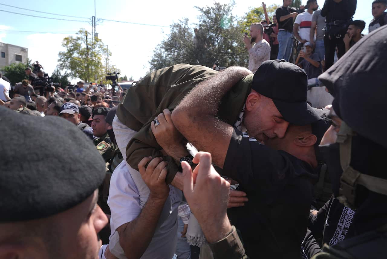 A crowd of people embrace a man who is sitting on another man's shoulders, visibly emotional.