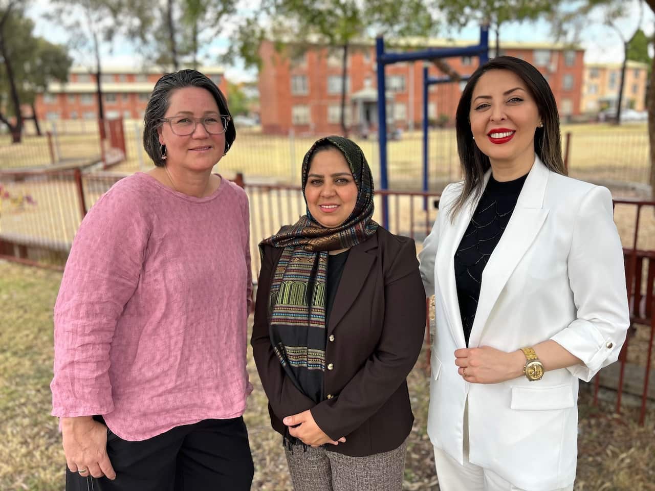 Three woman stand in a grassy field in front of a playground.