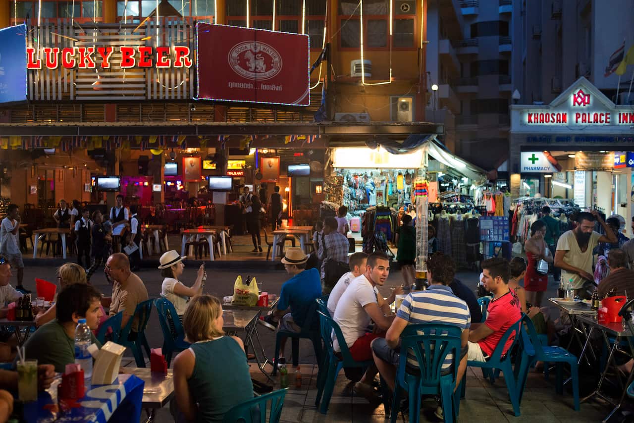 Tourists on plastic chairs at an outside food stall in Bangkok.