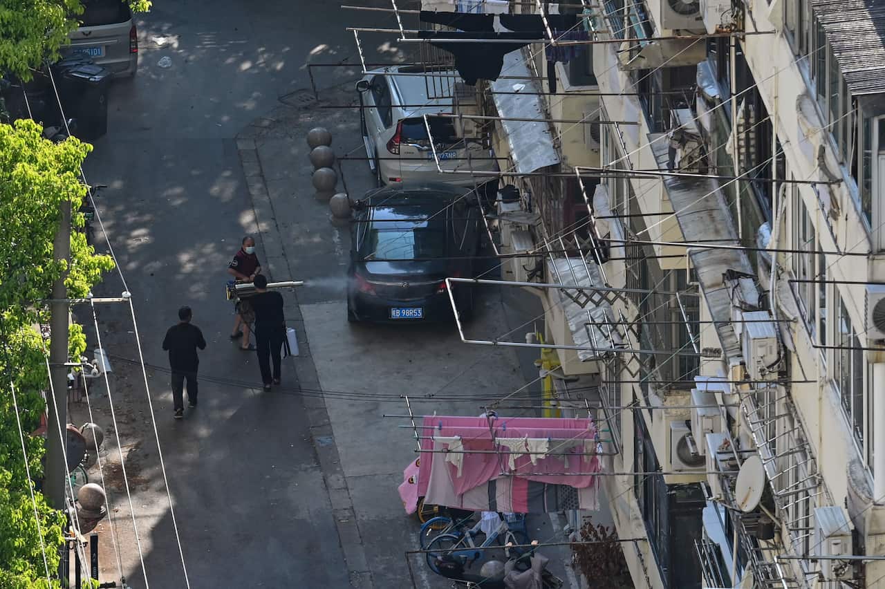 Two people walking behind a man who is spraying disinfectant on a street.