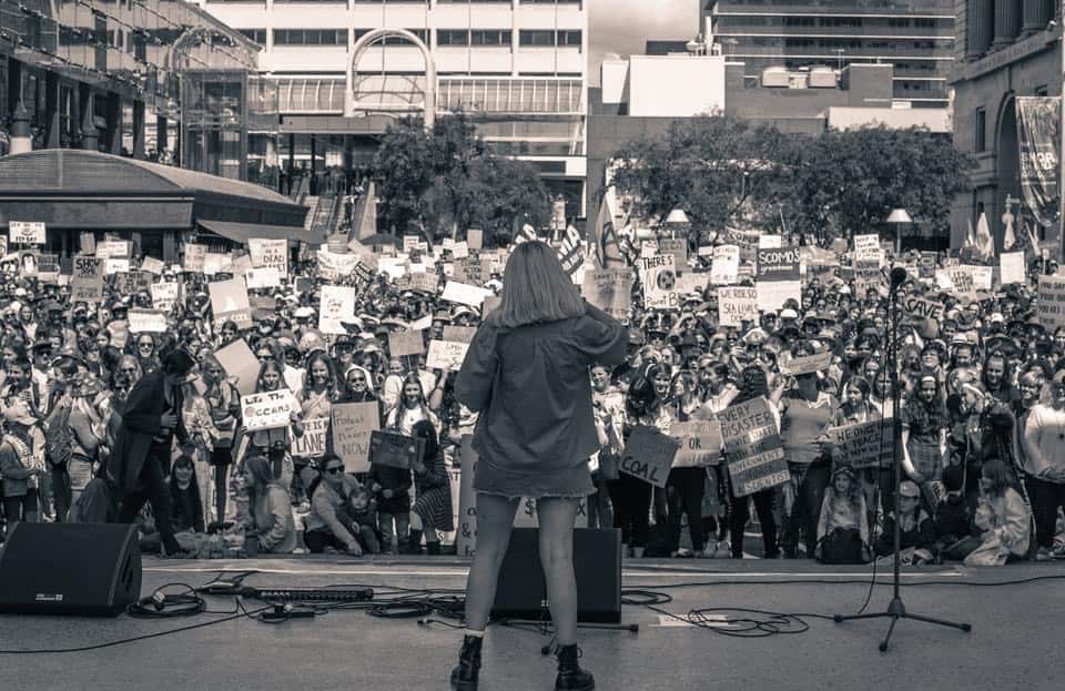 A young woman speaks on a stage in front of protesters. 