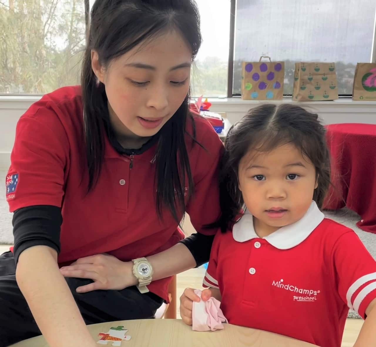 A woman in a red t-shirt sits next to a young girl at a table.