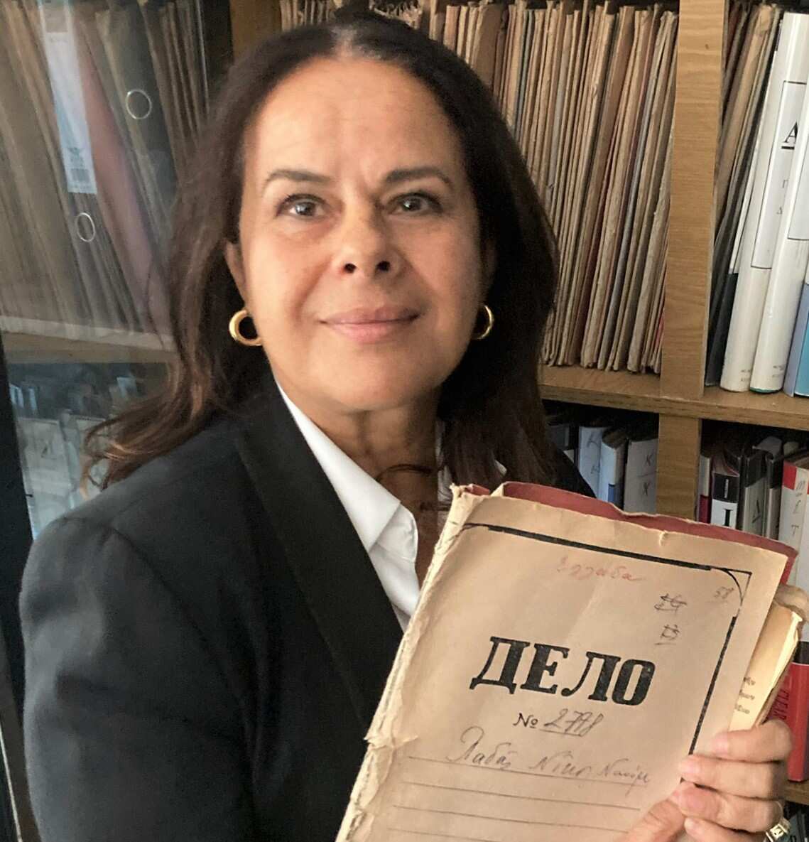 A portrait of Helen Vatsikopoulos holding some papers, looking at the camera. 