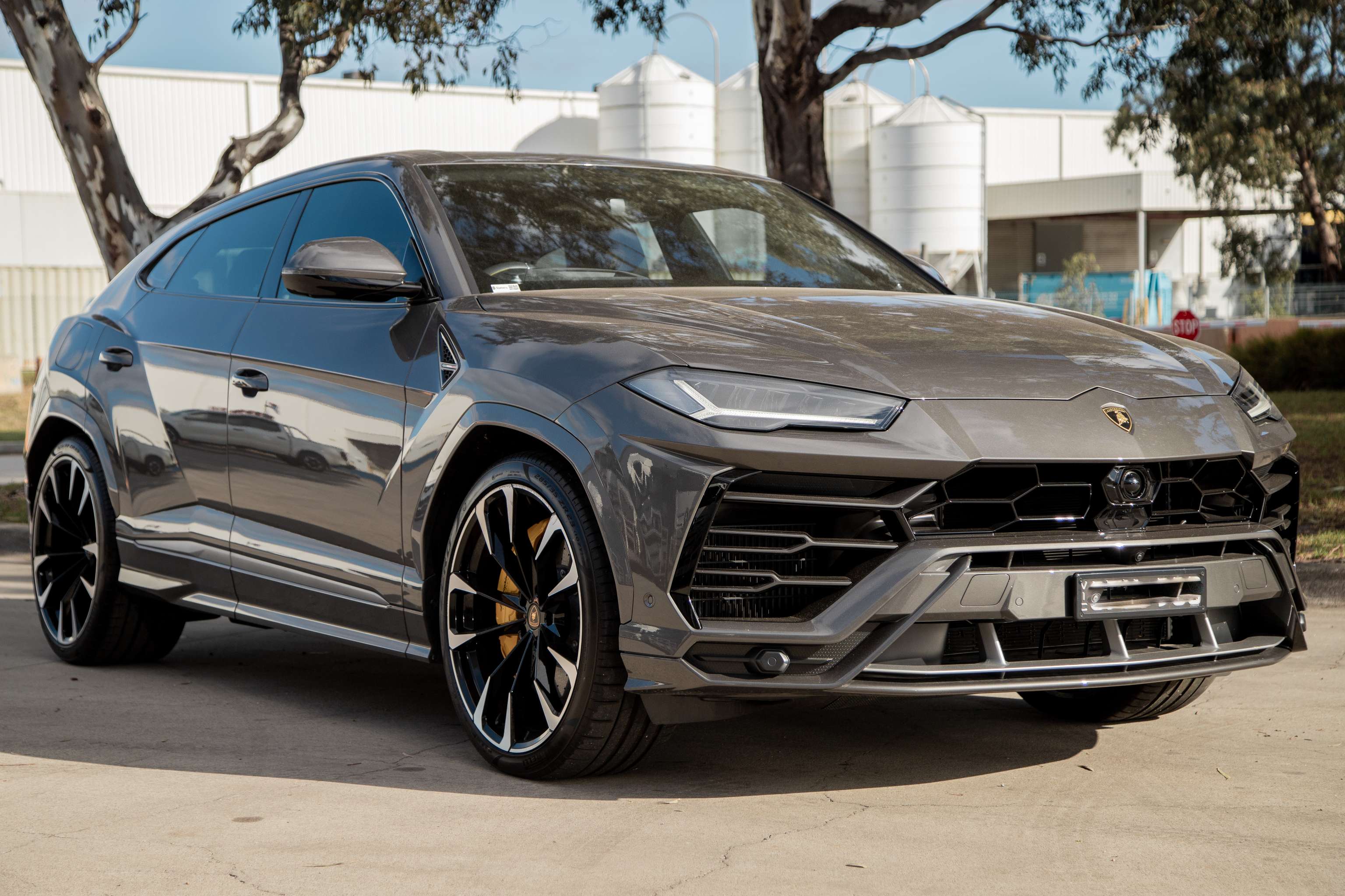A shiny grey Lamborghini SUV sits in front of a white industrial building. 