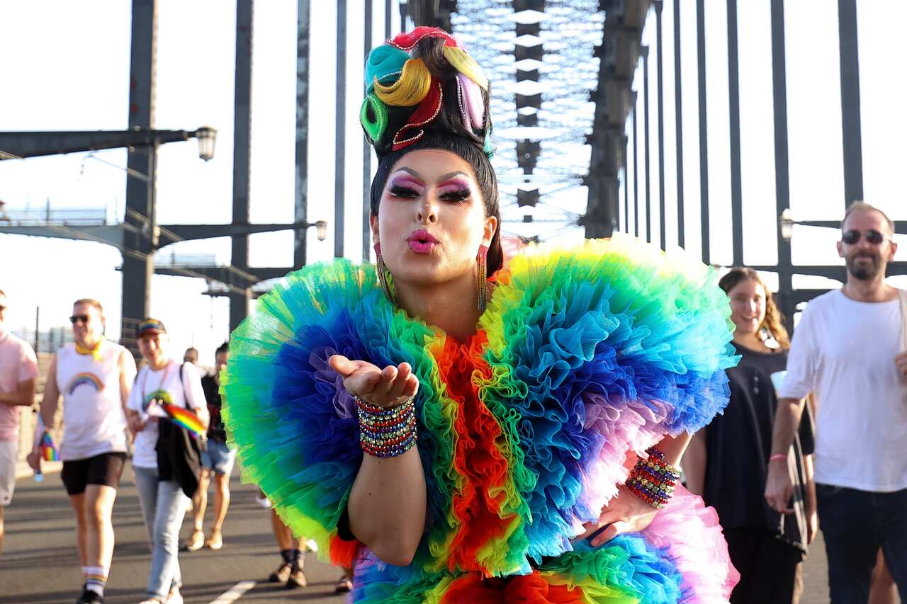 A drag queen dressed in rainbow-coloured clothes blows a kiss while walking across the Sydney Harbour Bridge