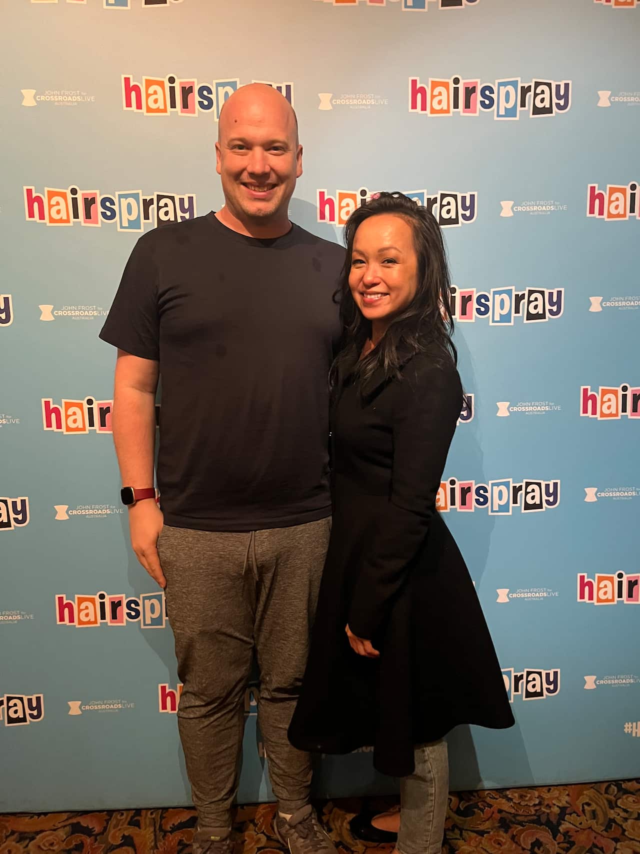 A man and a woman stand close together, smiling for the camera.