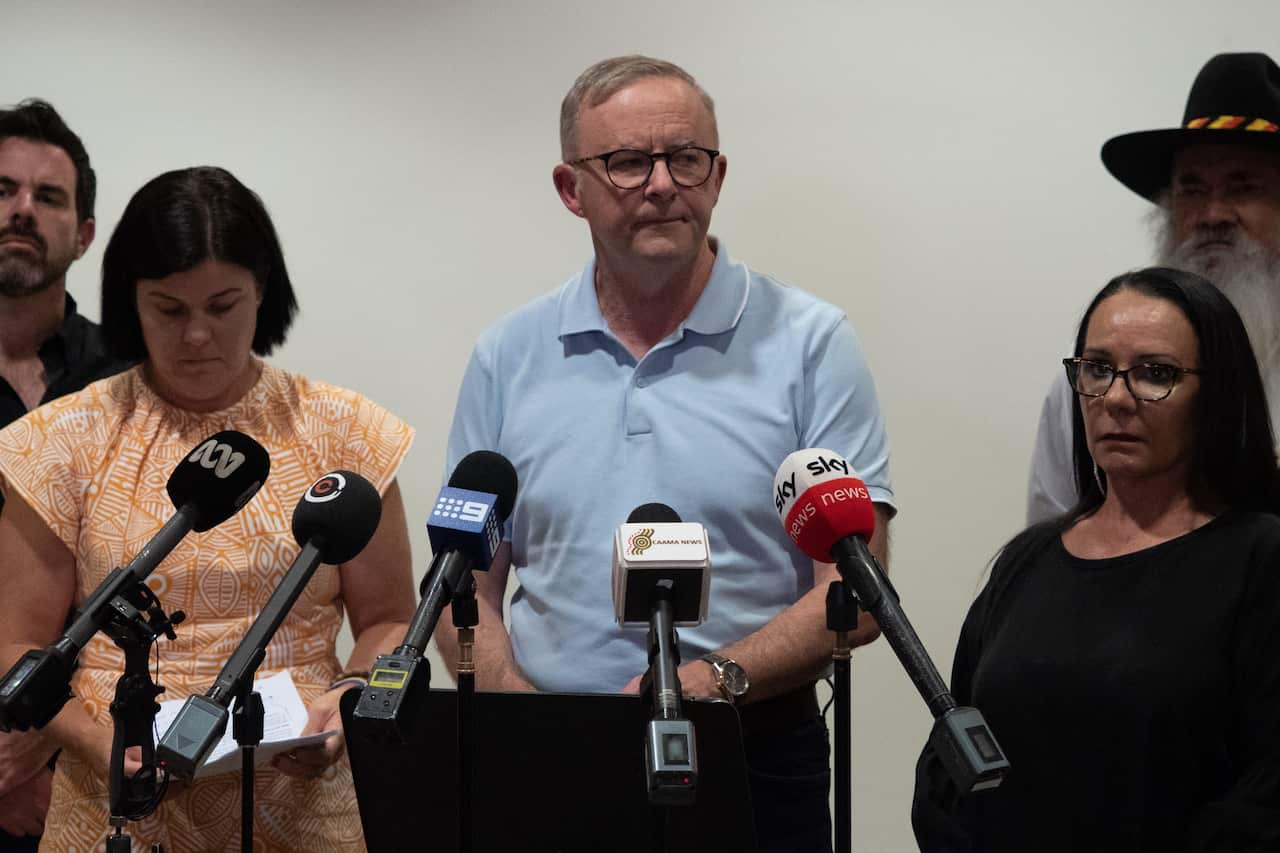 A man in a blue short-sleeved shirt speaks to the media 