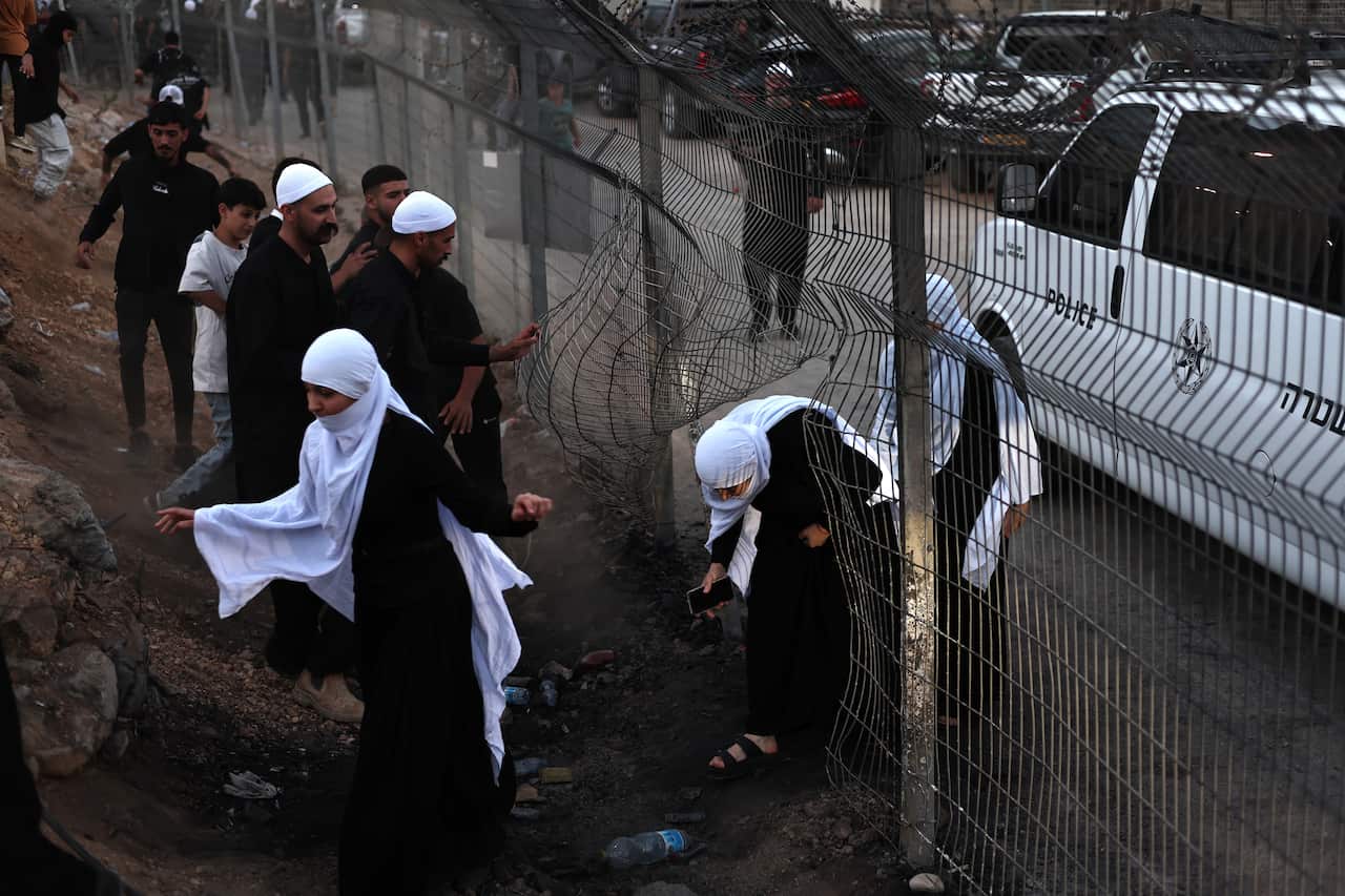 People climb under a broken wire fence.
