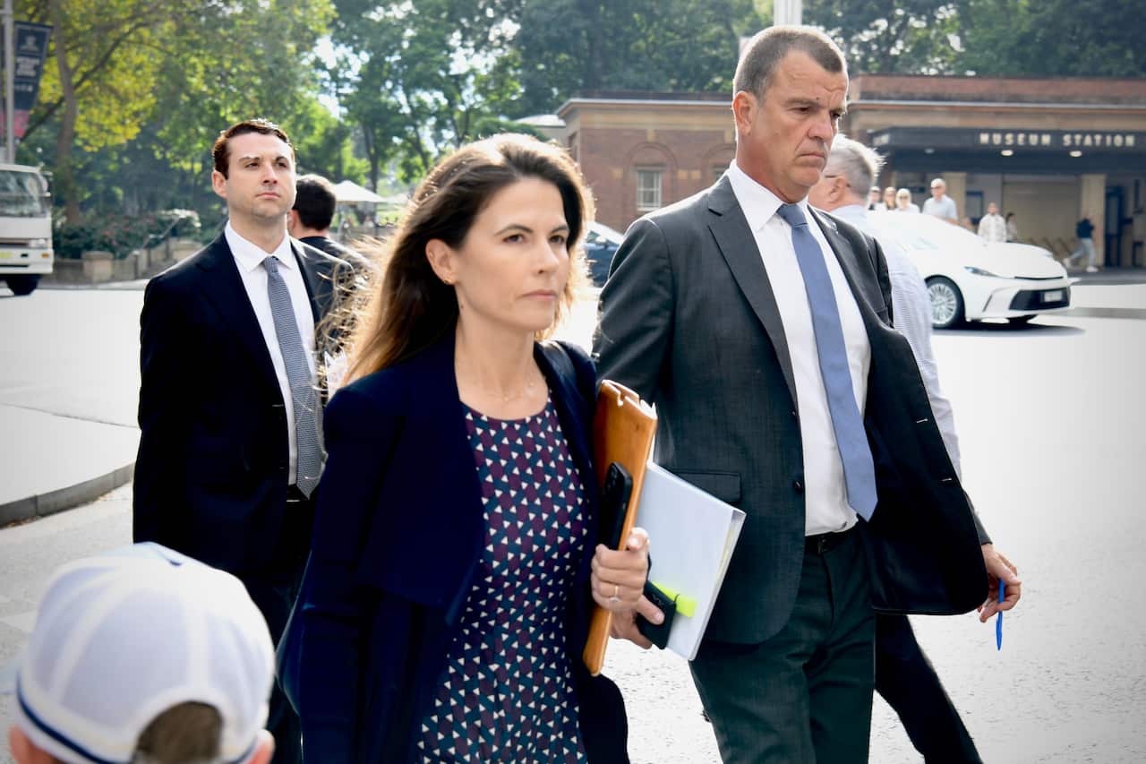 A smartly dressed woman and two men in suits walks across the road.