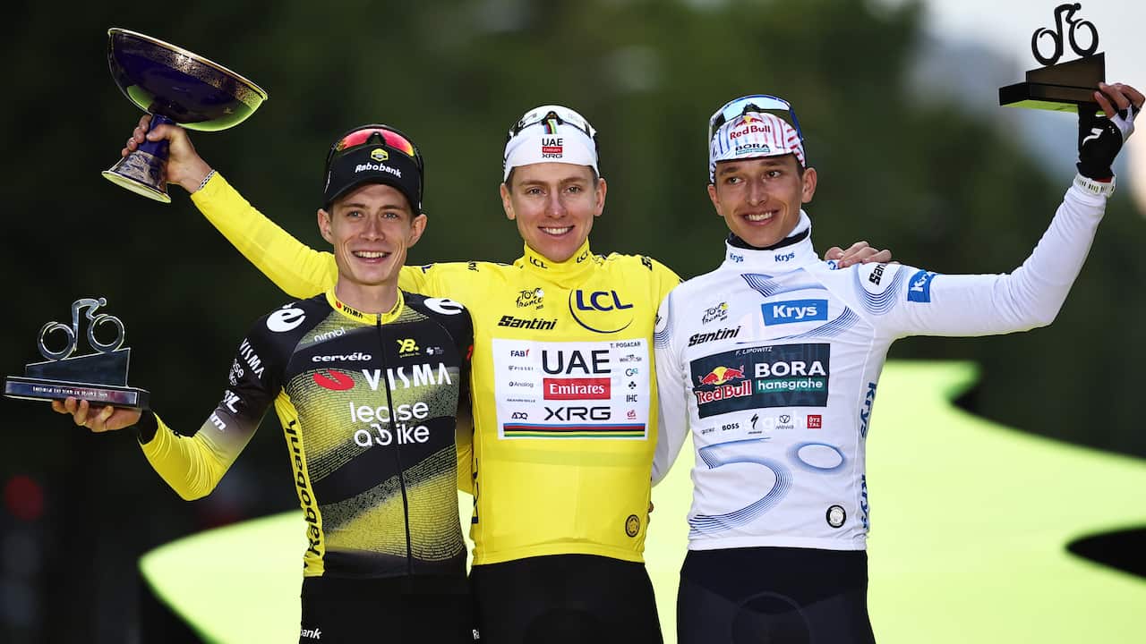 Three men in cycling gear stand on a podium, arms around each other, holding trophies in their free hands.