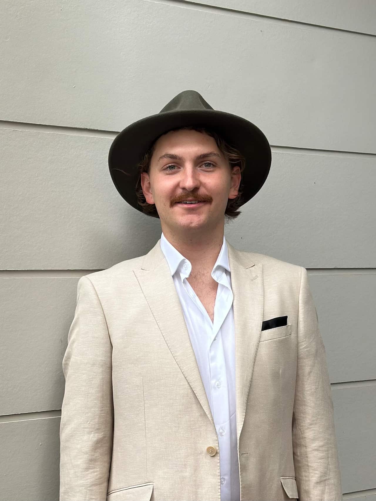 A young man wearing a suit and hat smiles at the camera.
