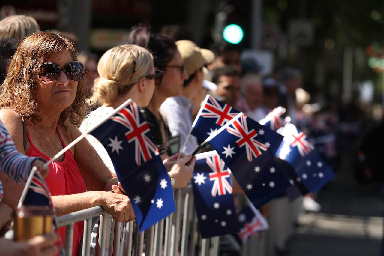 People hold little Australian flags along a barricade. 