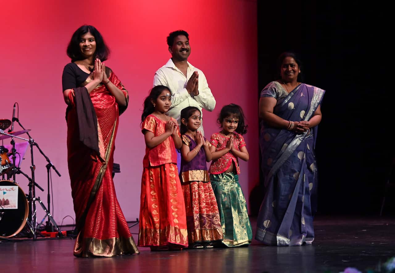 A man, two women and three children stand smile on stage.