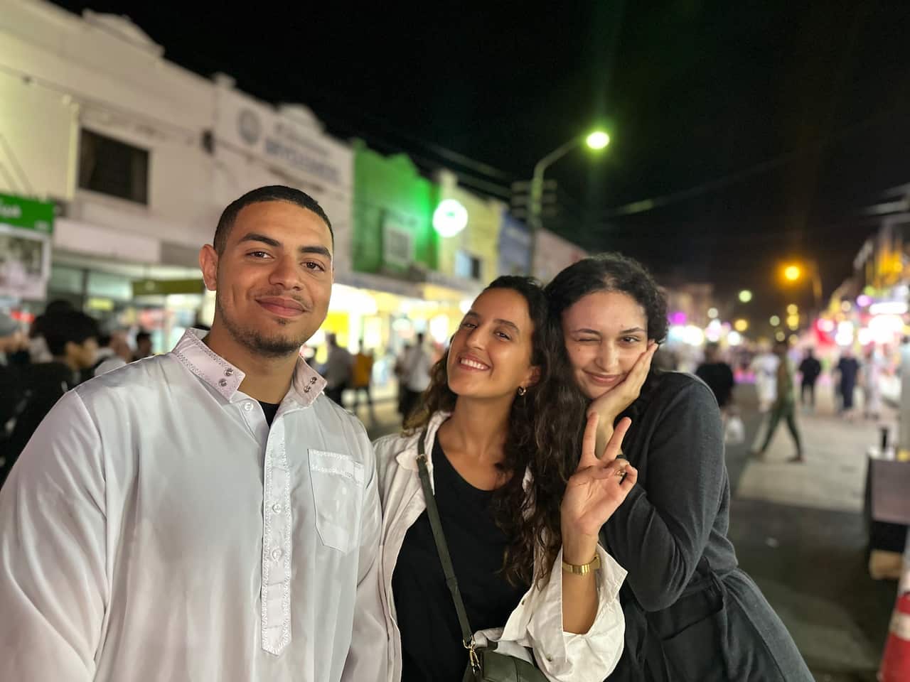 A man and two girls pose on a street at night. 