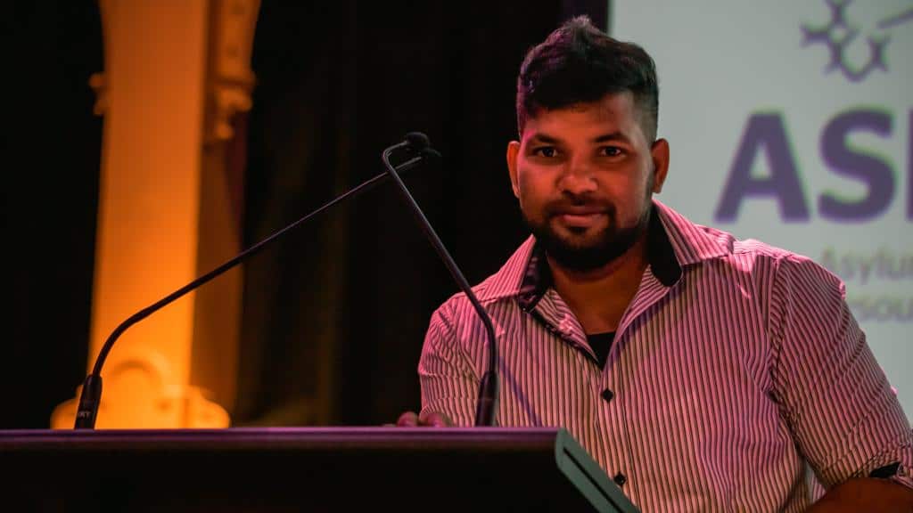 Sri Lankan refugee Thanush Selvarasa standing at a podium.