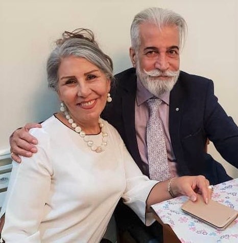 A woman with a white top sits next to a man with a grey beard.