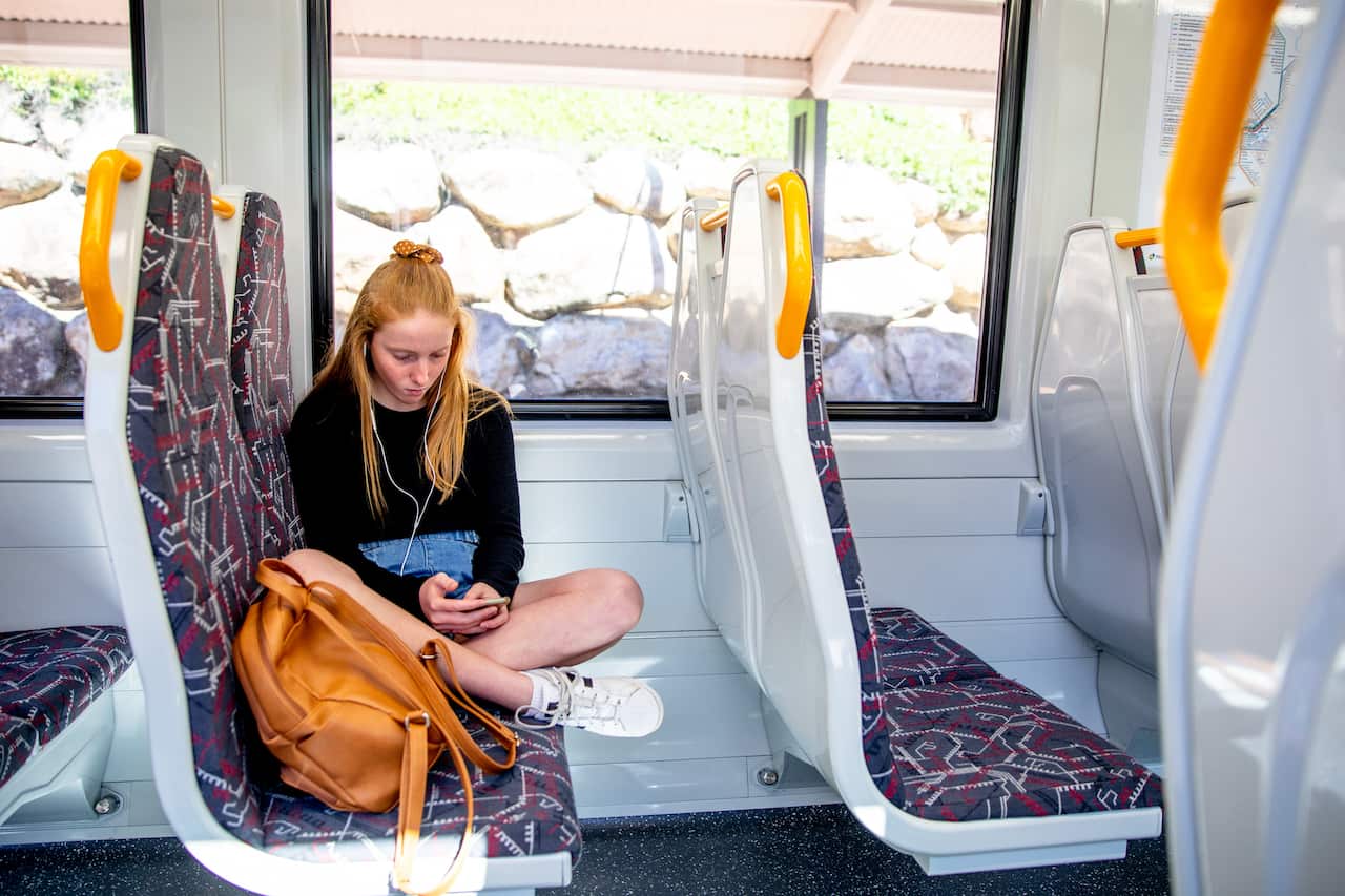 Teen girl with red hair tavels on the train listening to music and looking at her mobile phone