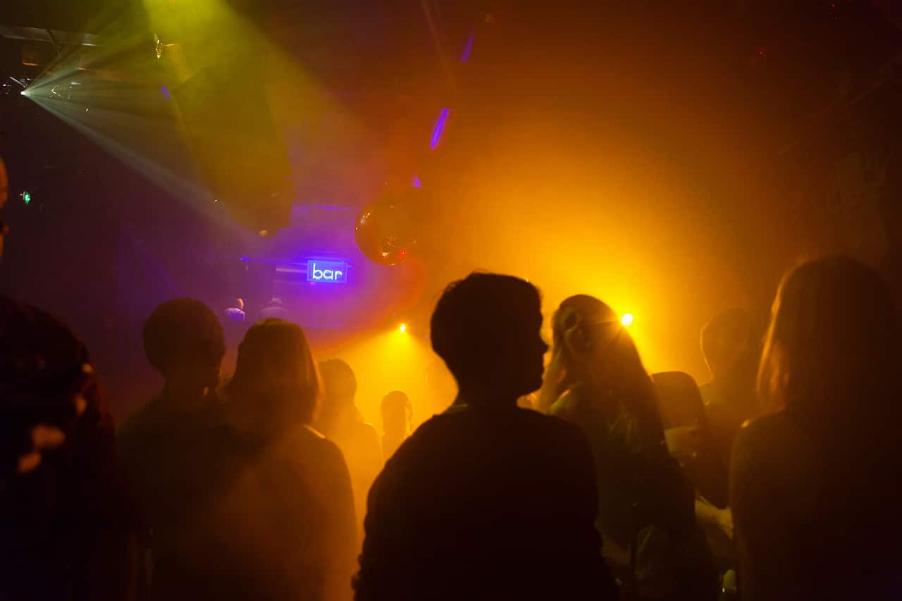 Nightclub scene with people dancing, a disco ball, and lighting equipment.