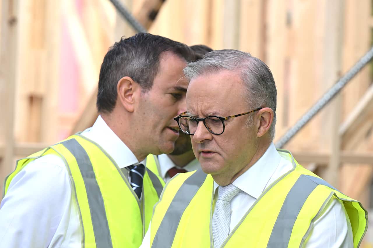 Anthony Albanese is wearing a hi vis vest as another man in hi vis vest walks behind him. 