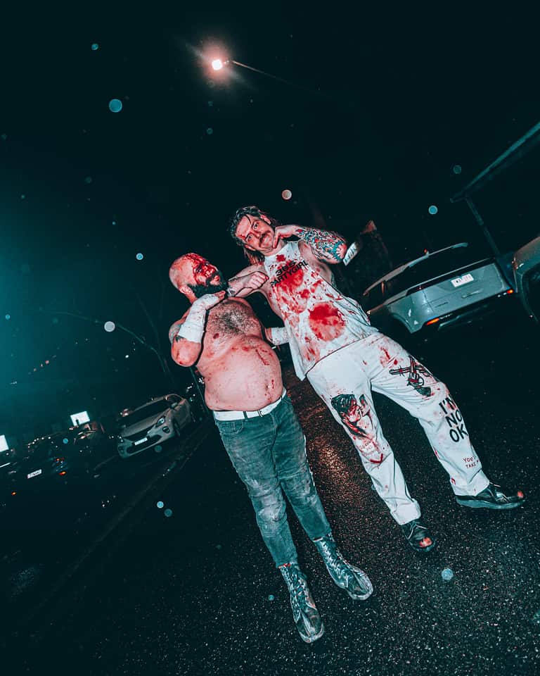 Two men smiling in a street while covered in blood. 