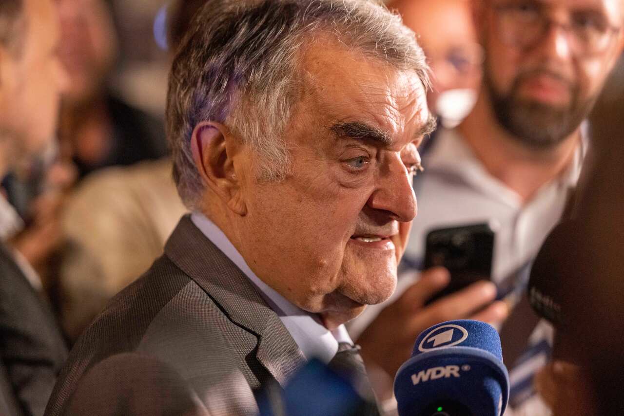 A man speaking into a blue press microphone. Others are surrounding him in the background.