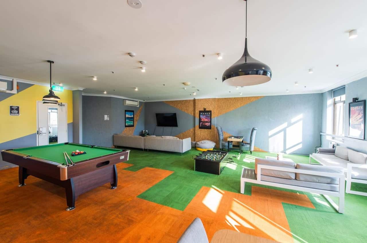 A living room with green and orange carpet, a pool table, couches and other furniture