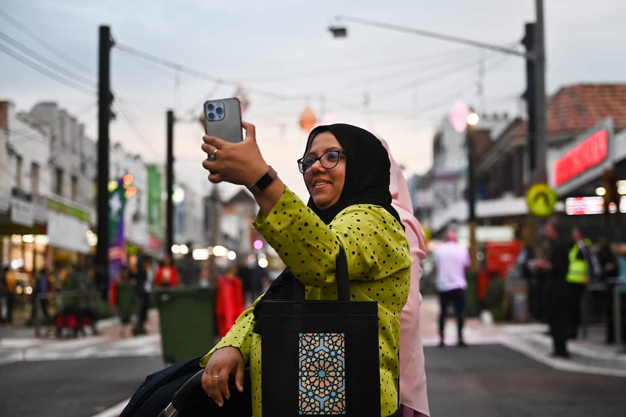 A woman in a yellow dress and a black scarf takes a selfie.