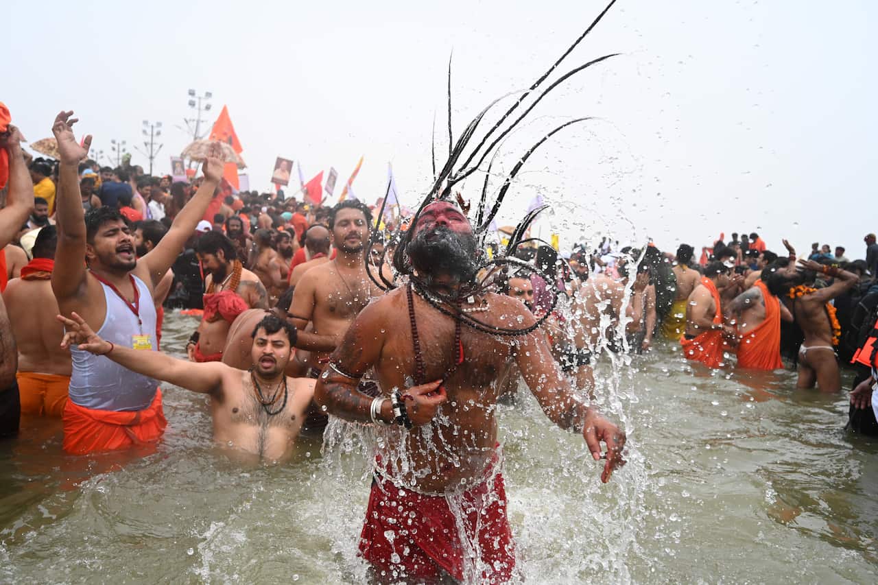 A man wearing a red loincloth submerged up to his thighs in water flicks his long hair back.