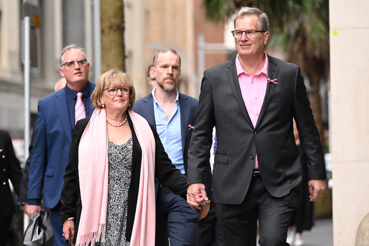 A woman and a man walk while holding hands.