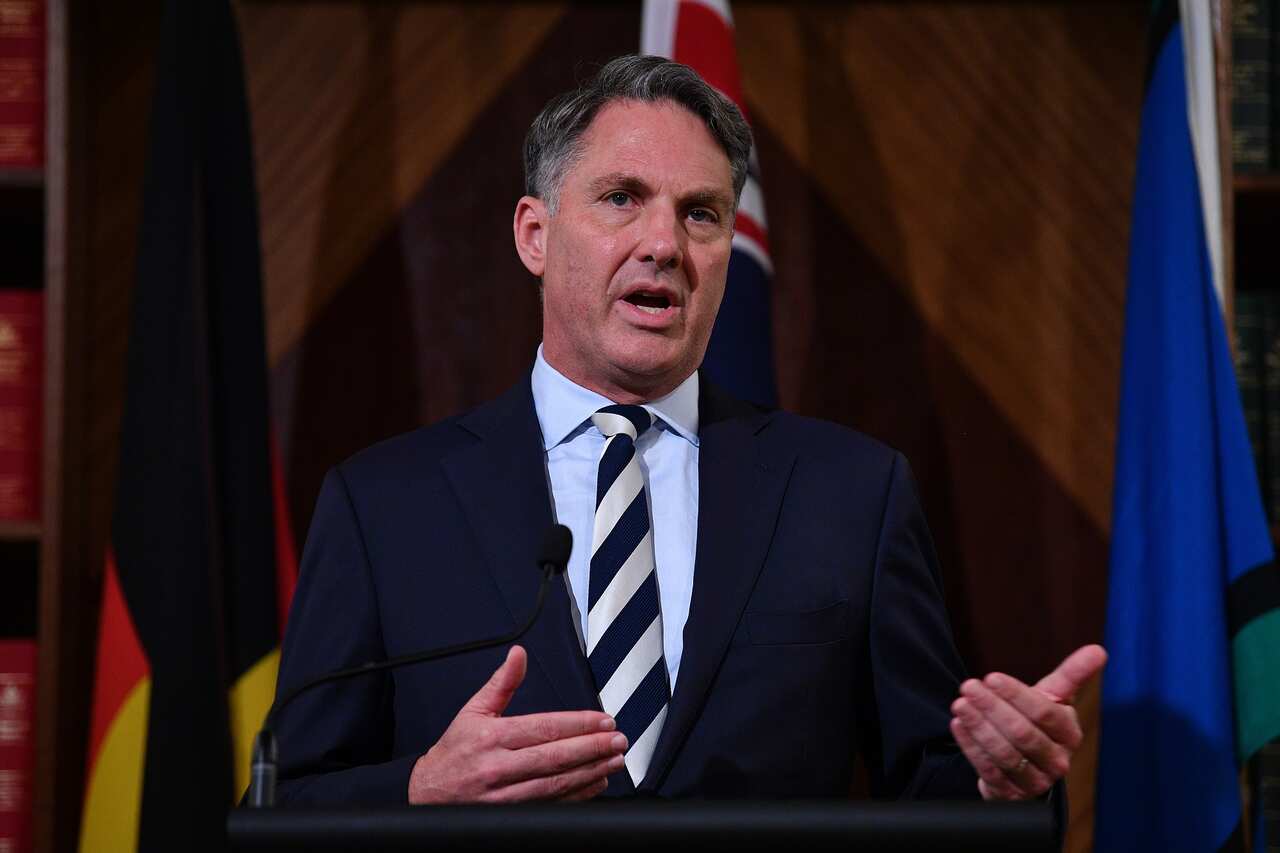 Australia's Defence Minister Richard Marles stands in front of the Australian flag, the Aboriginal flag and the Torres Strait Islander flag. 