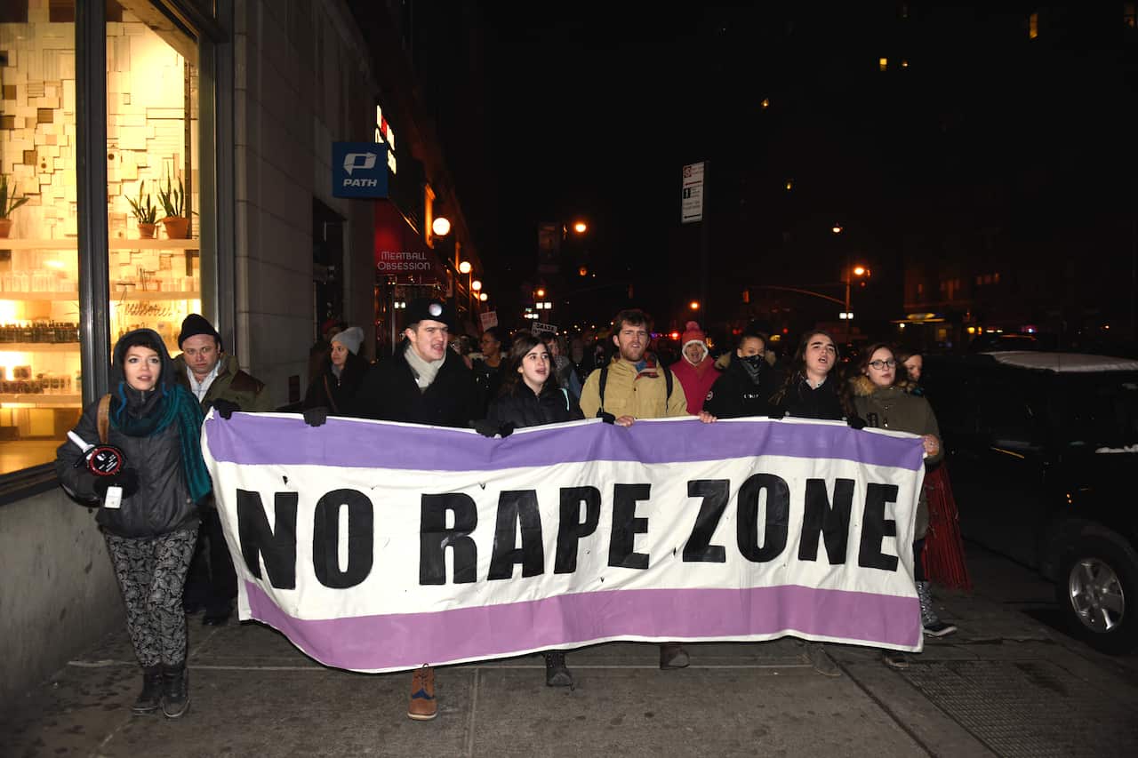 A group of men and women holding a purple-and-white banner reading No Rape Zone march down the street in New York