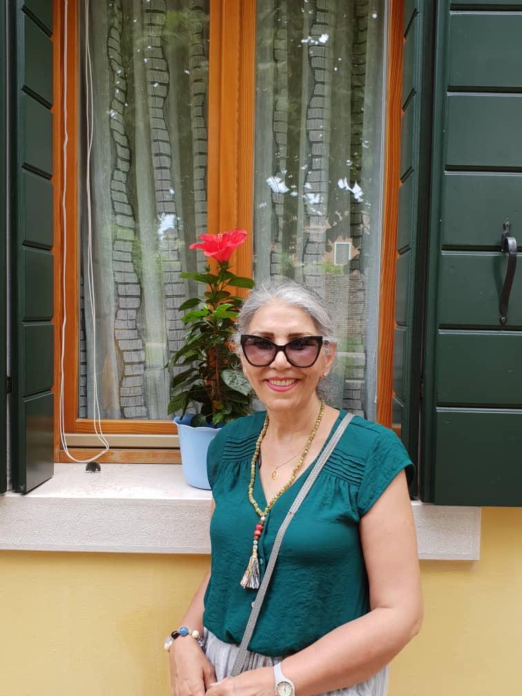 An elderly woman in a green top and sunglasses is smiling.