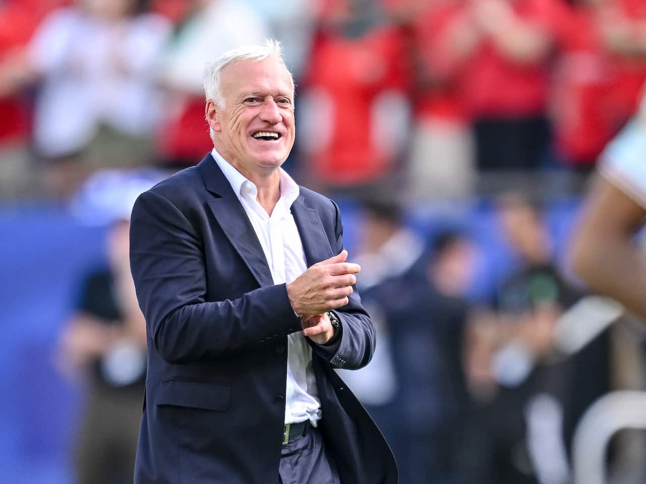 A middle-aged white man in a dark suit jacket and white shirt, smiling