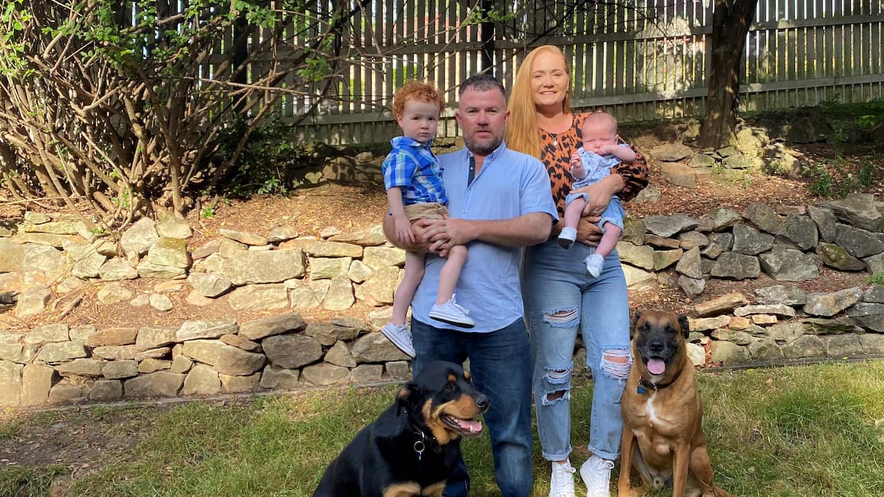 A man and woman with two young children and two dogs standing in a backyard