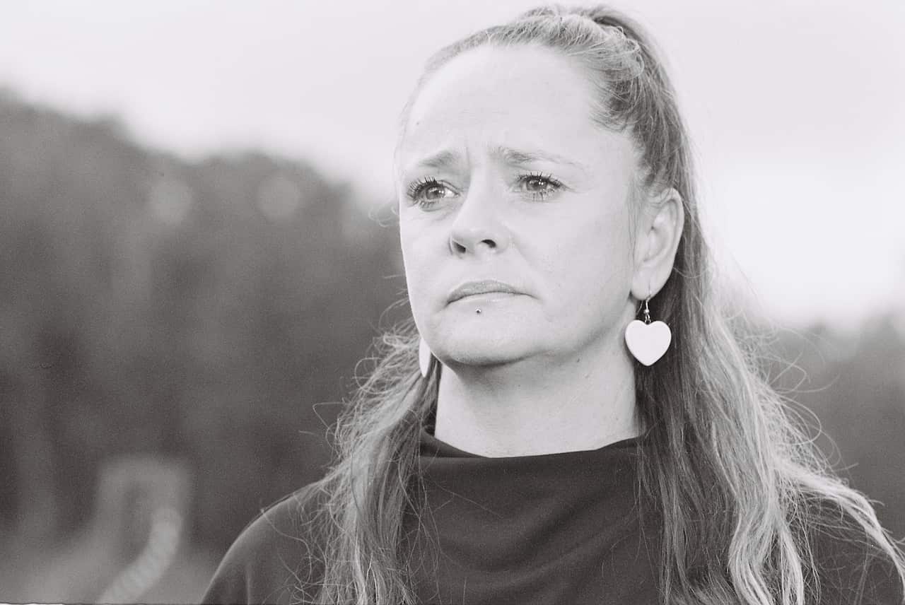 A black-and-white image of a woman in a black shirt and love-heart-shaped earrings looking serious.