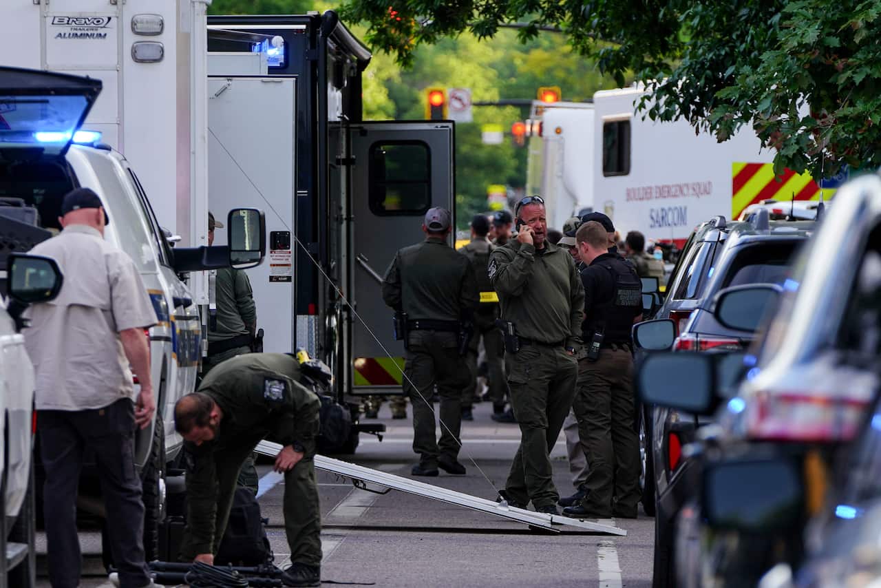 Law enforcement officers in between a row of parked vehicles, including an ambulance and police cars.