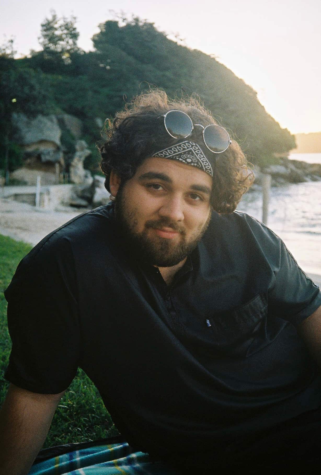 Man smiles in a black thawb near the water.