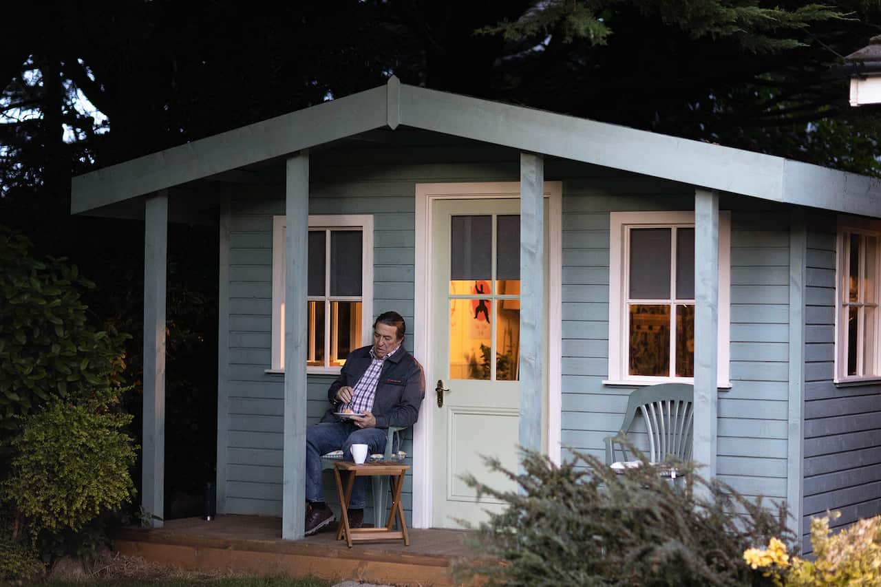 A man sits outside a small blue-painted building. 