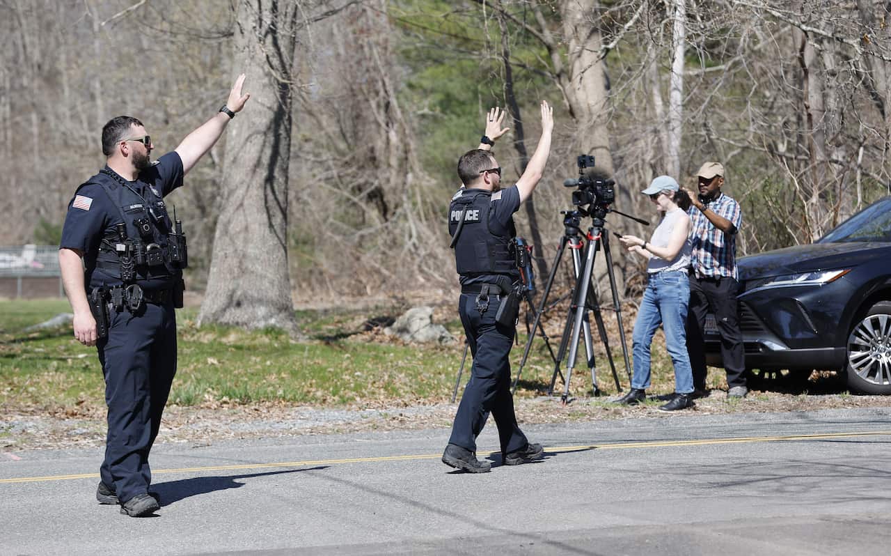 Two police officers dressed in navy blue uniforms hold their hands up in the air in attempt to block vehicles from coming down the road.