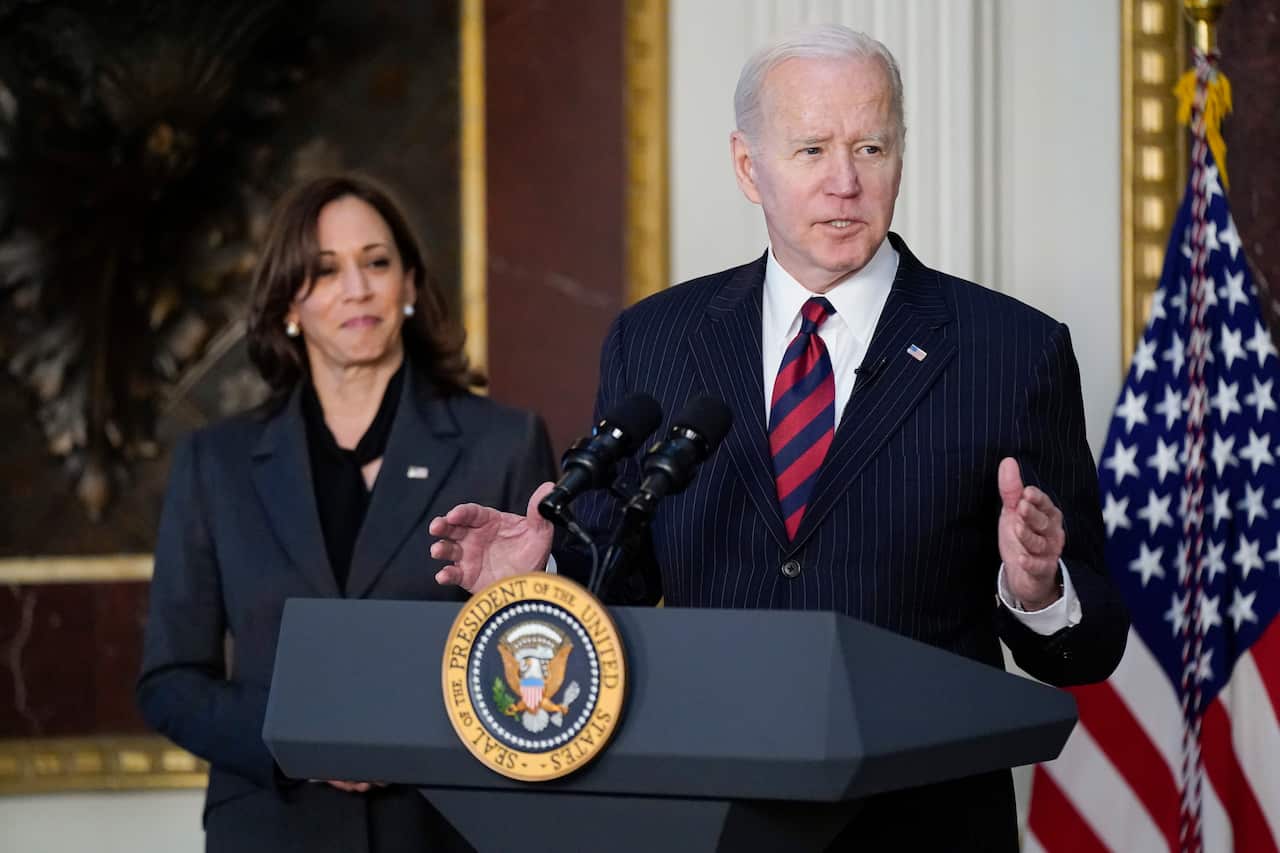 Joe Biden is speaking at a podium, in front of an American flag. Kamala Harris is behind him.