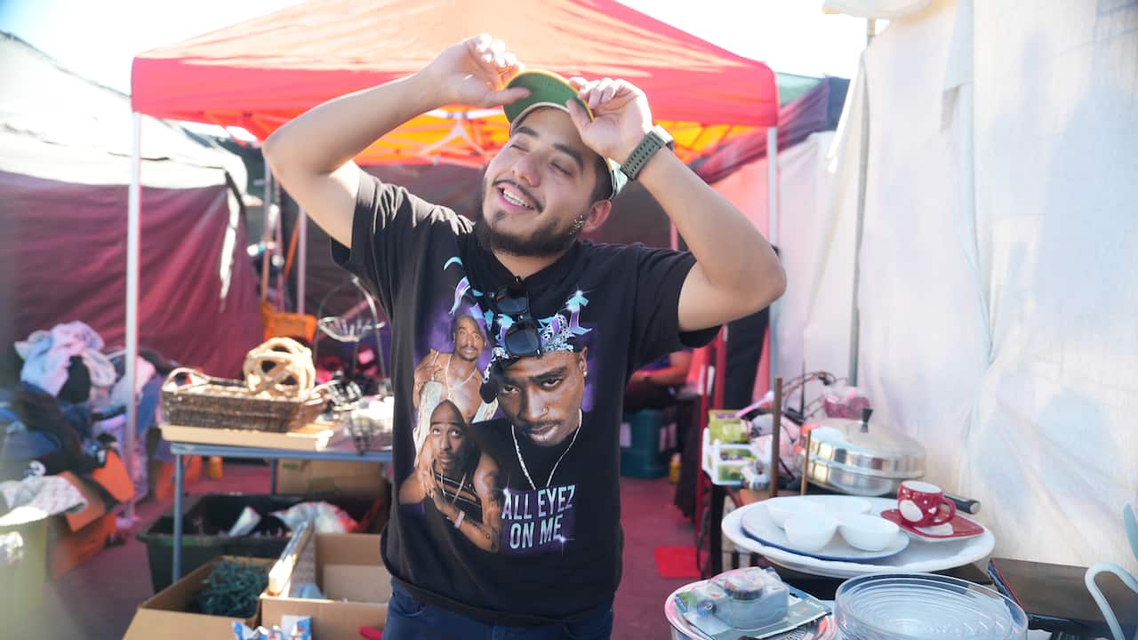 A man in a round black t-shirt featuring pictures of a rapper smiling while holding his cap.