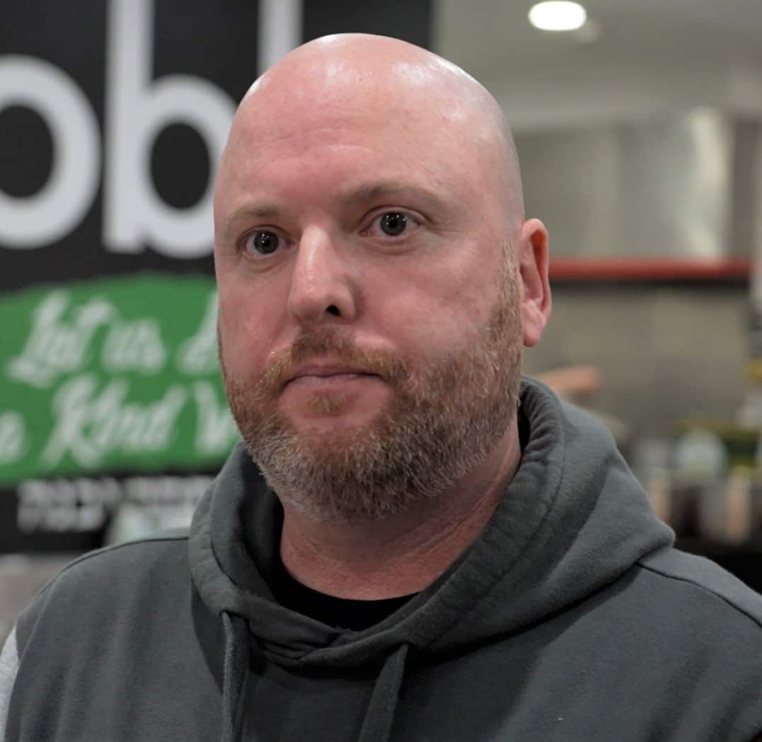 A man in a grey hoodie stands inside a commercial kitchen.